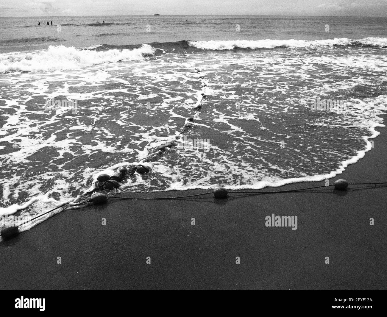 Bouées sur une corde près de l'eau de mer. Les bouées de sauvetage se contentent d'alerter les gens de la profondeur de l'eau. Délimitant un lieu sur une plage de sable entre les hôtels. Vague avec des bulles. Photo noir et blanc monochrome Banque D'Images