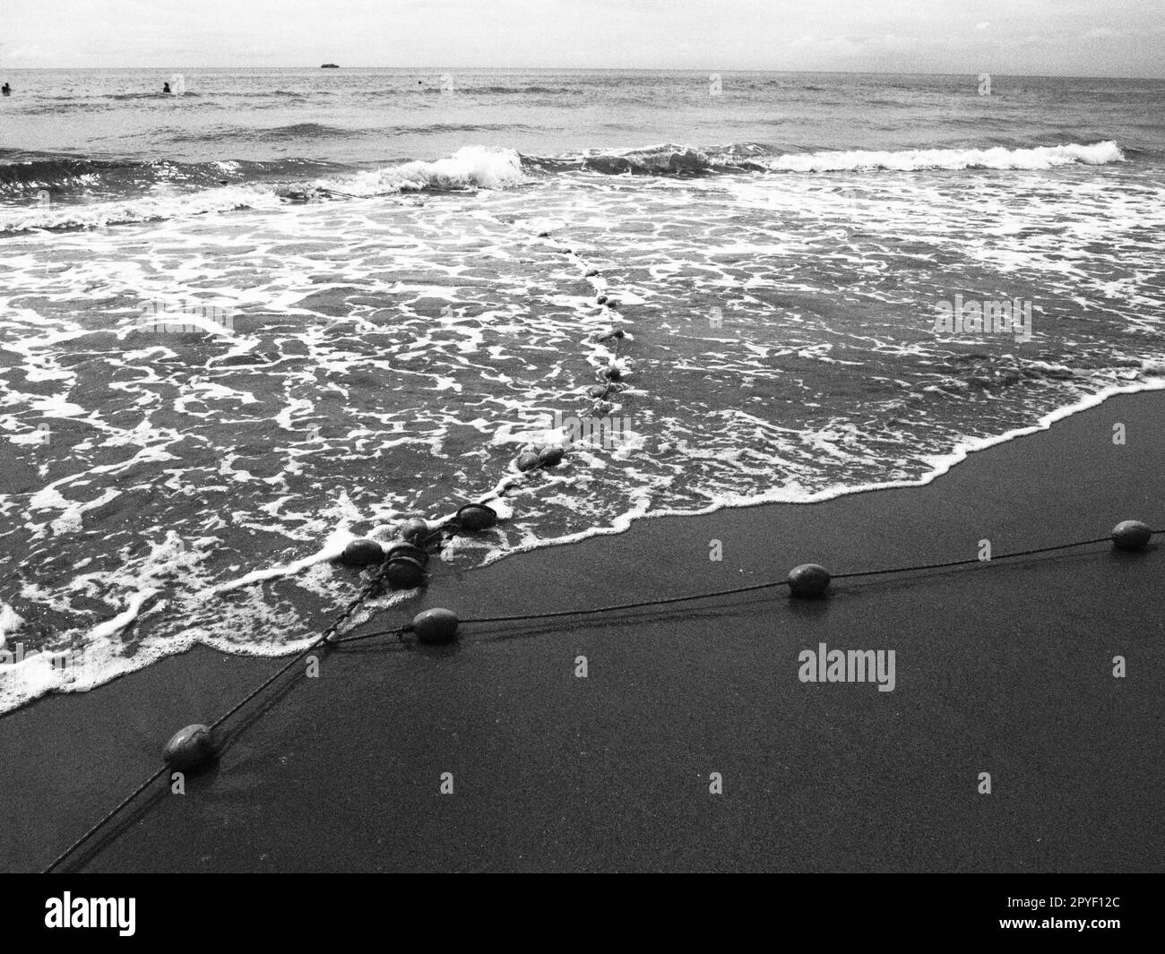 Bouées sur une corde près de l'eau de mer. Les bouées de sauvetage se contentent d'alerter les gens de la profondeur de l'eau. Délimitant un lieu sur une plage de sable entre les hôtels. Vague avec des bulles. Photo noir et blanc monochrome Banque D'Images