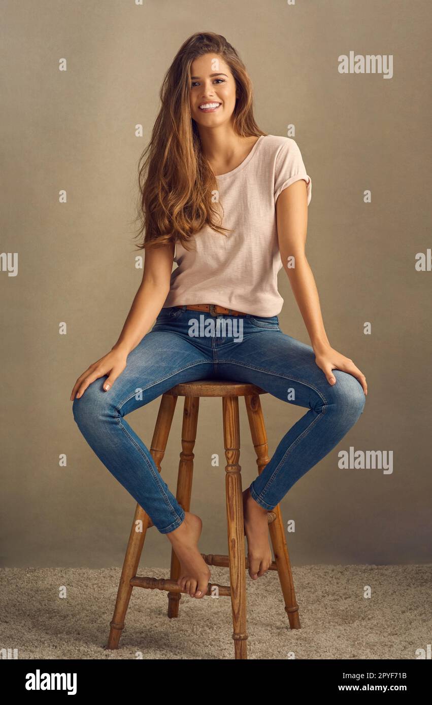 Être heureux ne passe jamais par le style. Photo studio d'une belle jeune femme assise sur un tabouret sur un fond plat. Banque D'Images