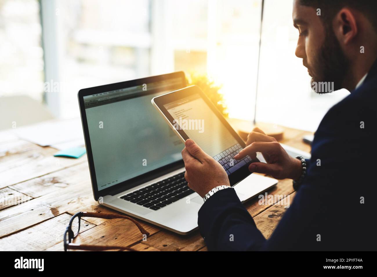 Numérisation de sa liste de tâches. un jeune homme d'affaires utilisant une tablette numérique et un ordinateur portable à son bureau. Banque D'Images