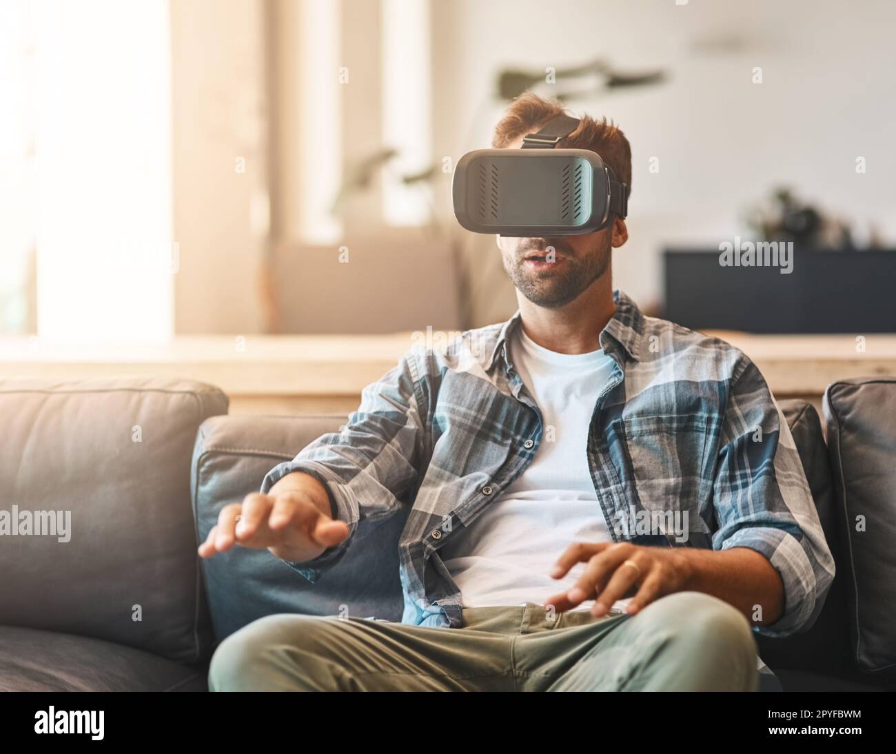 Divertissement pour tous les sens. un jeune homme utilisant un casque de réalité virtuelle sur le canapé à la maison. Banque D'Images