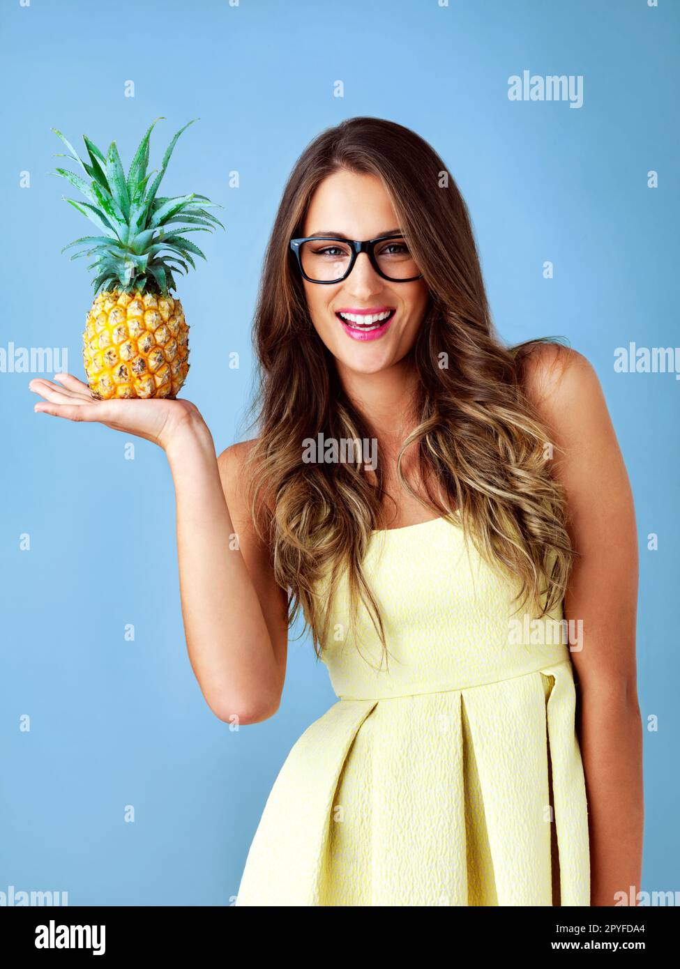 Il est très piquant à l'extérieur mais doux à l'intérieur. Photo studio d'une jeune femme tenant un ananas sur fond bleu. Banque D'Images