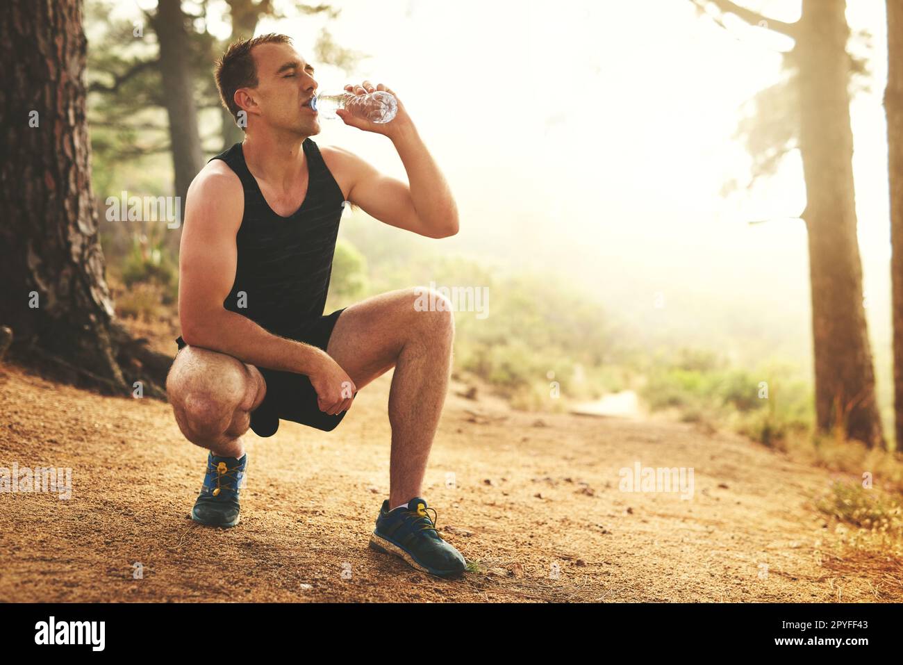 Lui faire le plein d'énergie. un jeune homme sportif boit de l'eau pendant qu'il est en train de courir dans la forêt. Banque D'Images