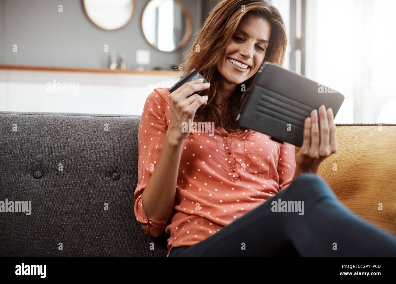 Moins de files d'attente, plus de confort. une jeune femme attrayante utilisant une tablette numérique et une carte de crédit sur le canapé à la maison. Banque D'Images