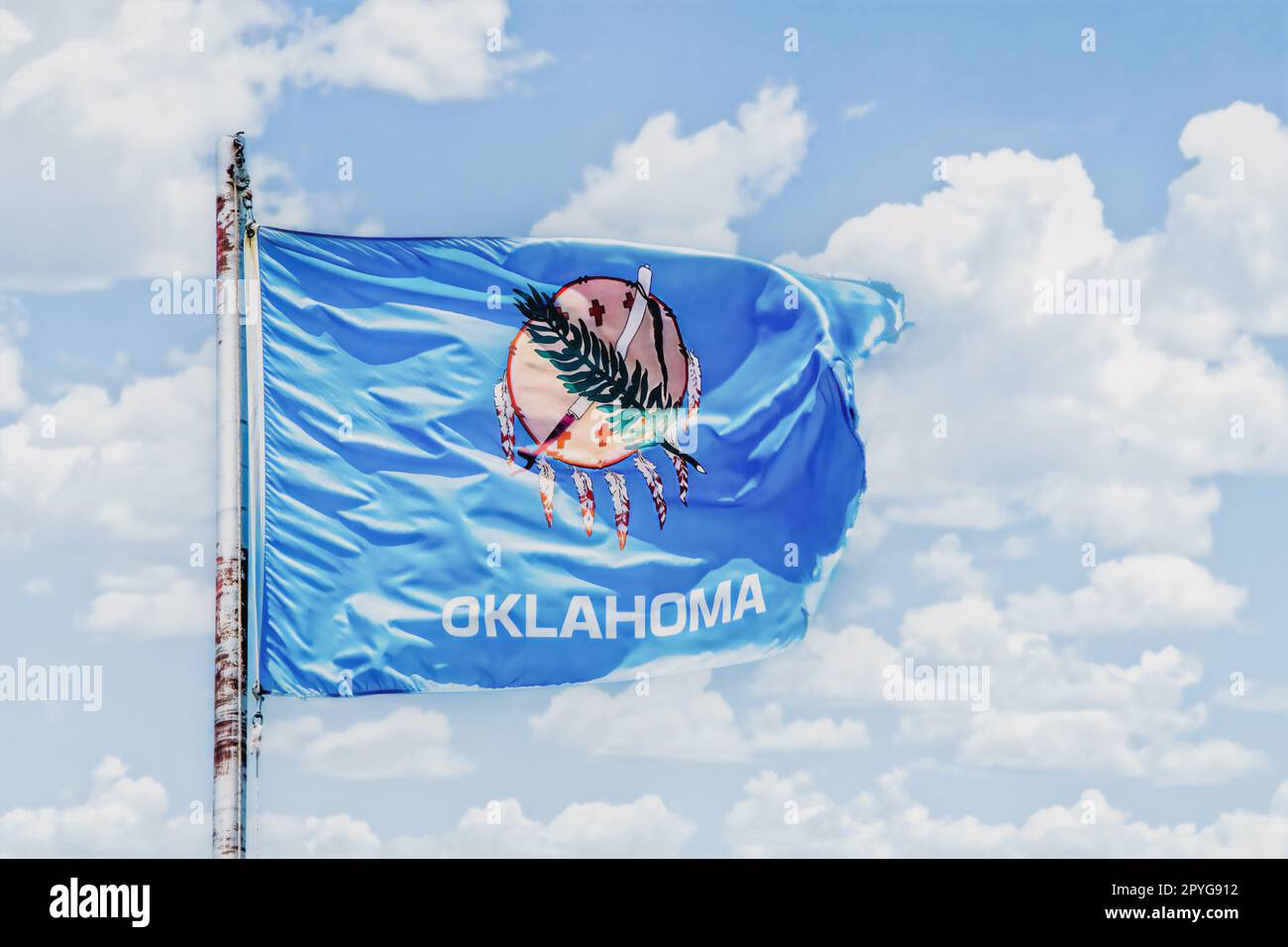 Drapeau de l'Oklahoma volant dans un ciel nuageux agitant sur un mât rouillé - État des États-Unis Banque D'Images