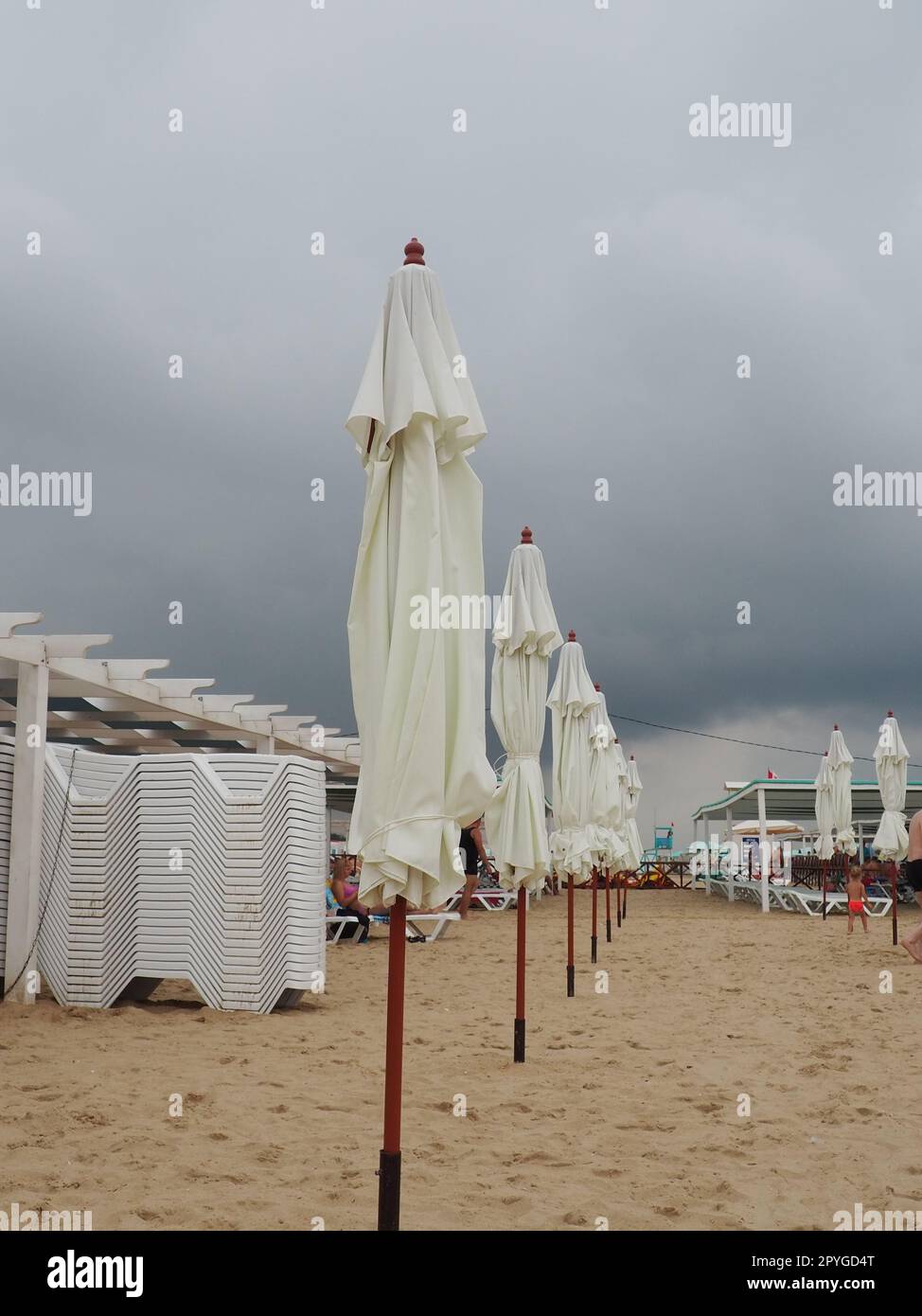 Transats humides et parasols sur la plage de la mer pendant la tempête de pluie forte. Parasol roulé sur la plage contre le ciel nuageux sombre. Invasion d'un typhon, d'un cyclone ou d'une tempête sur la mer ou l'océan. Saison de plage Banque D'Images