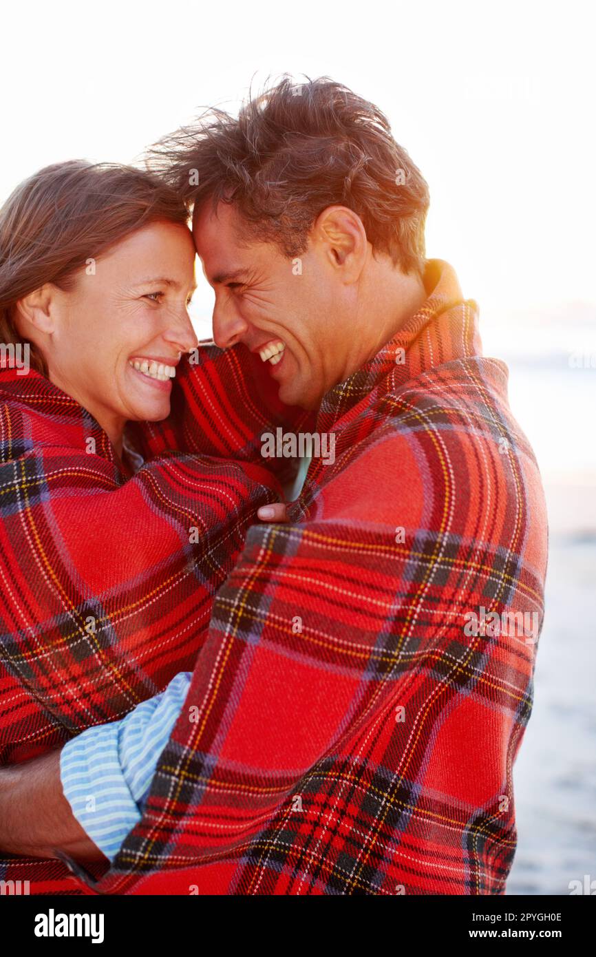 Vous seul... Un couple dévoué et affectueux enveloppé dans une couverture sur la plage. Banque D'Images