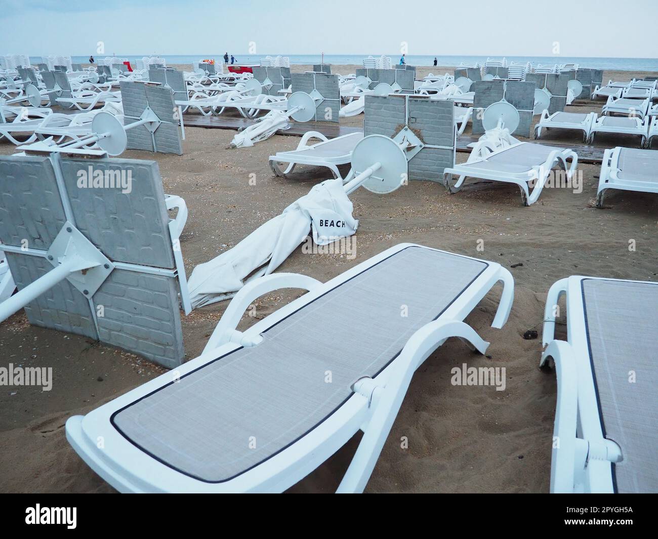 Un parasol était plié sur une plage de sable fin après le mauvais temps. Tempête en mer. Fin de la saison des plages en raison du typhon et du cyclone. Chaises longues, parasols et mobilier d'hôtel. Structures renversées par le vent Banque D'Images