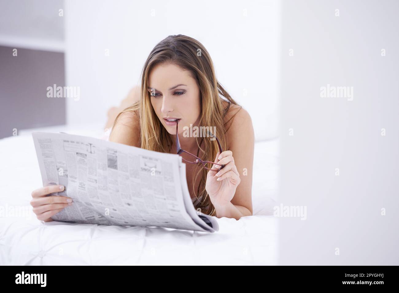 Suivi des événements en cours. Une jeune femme attrayante lisant le papier en étant allongé sur son lit. Banque D'Images