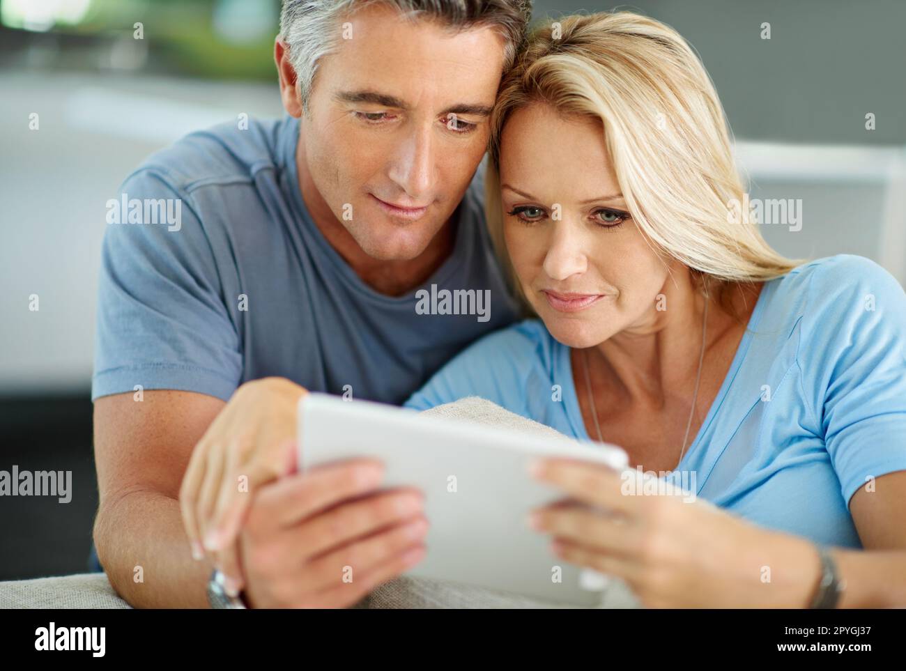 Voyons où nous devrions passer nos prochaines vacances... un couple souriant assis à la maison à l'aide d'une tablette numérique. Banque D'Images