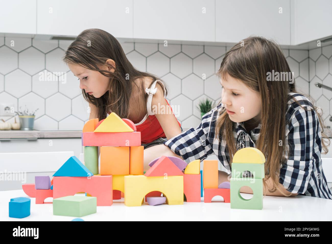 Sérieuses concentrées, concentrées petites filles jouant avec des briques colorées et des éléments de construction et des figures sur la table blanche Banque D'Images