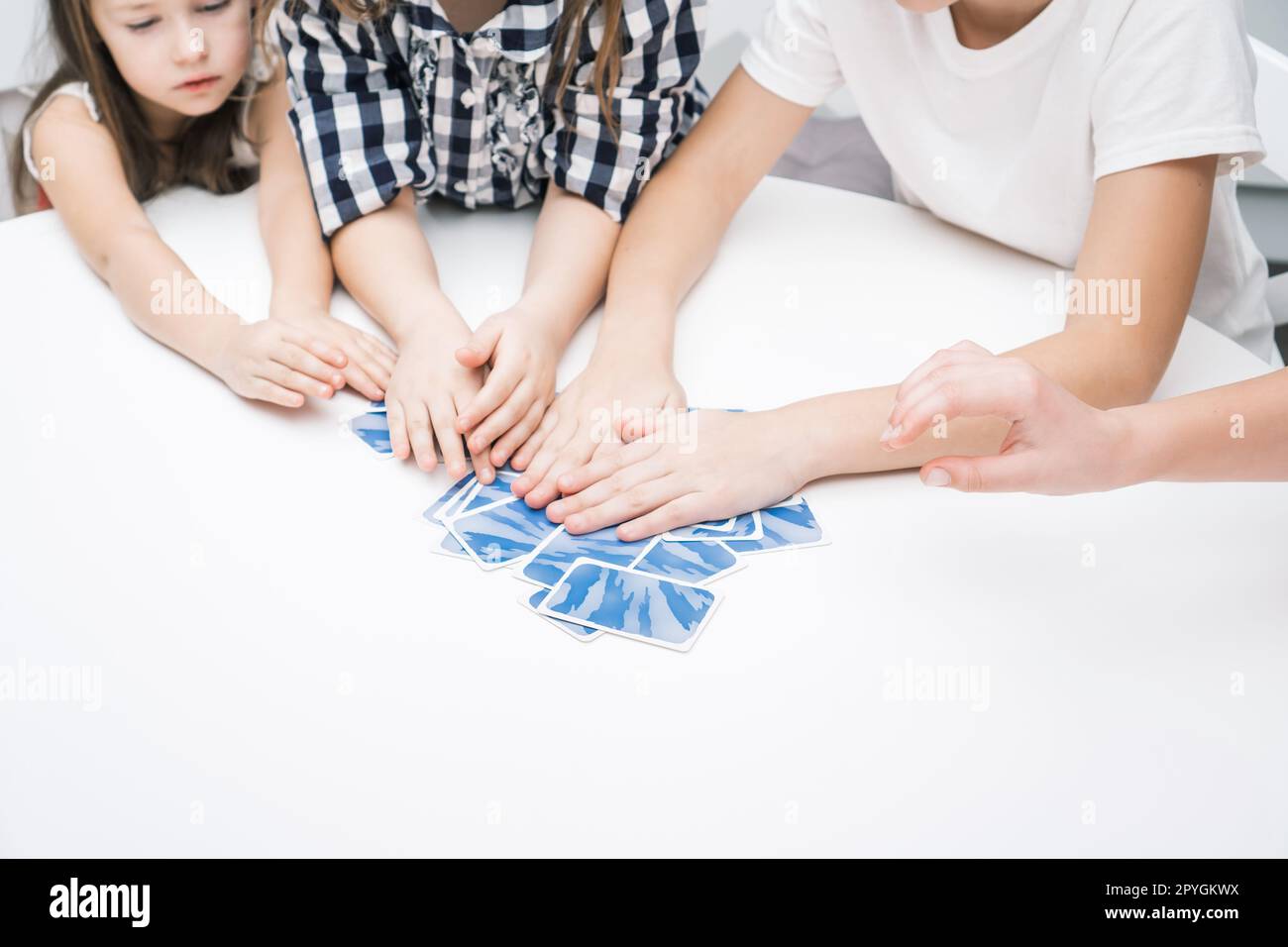 Les mains des enfants recadrées méconnaissables tiennent des cartes à jouer bleues sur la table blanche. Jeu intelligent pour le temps, qui d'abord. Amusement en famille Banque D'Images