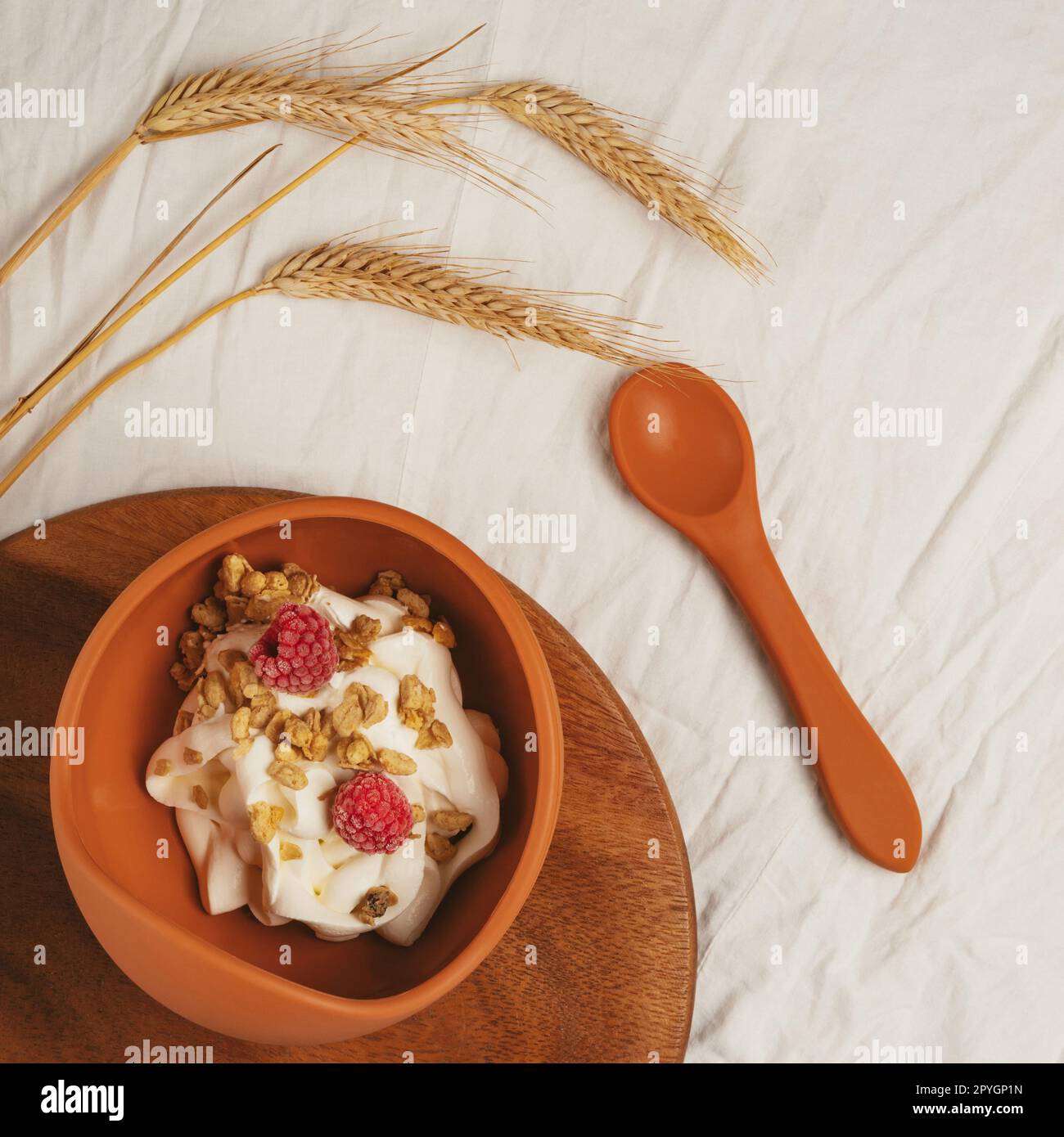 Bol moderne en silicone brun de granola avec yaourt, noix et paire de framboises mûres servi sur un plateau en bois avec cuillère. Banque D'Images