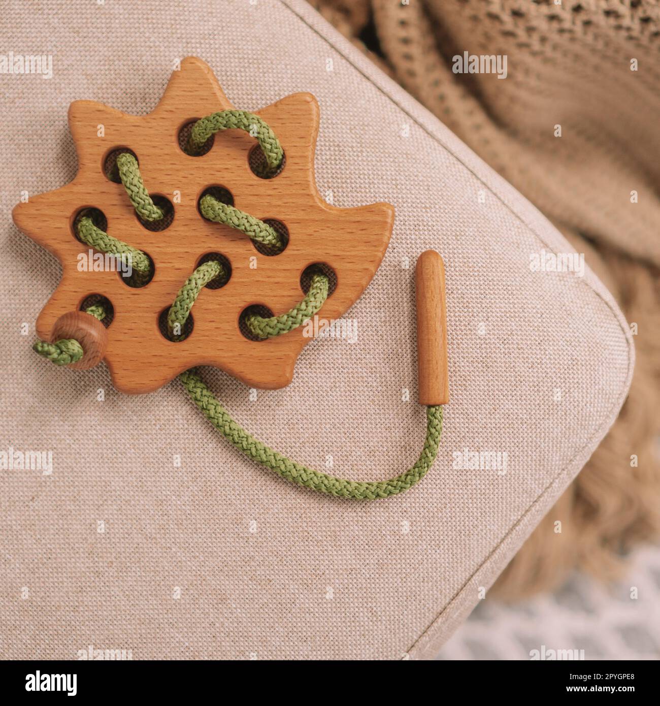 Jouet en bois pour enfants avec des trous pour apprendre le laçage avec cordon vert sur banc beige. Vue de dessus. Cadre carré instagram Banque D'Images