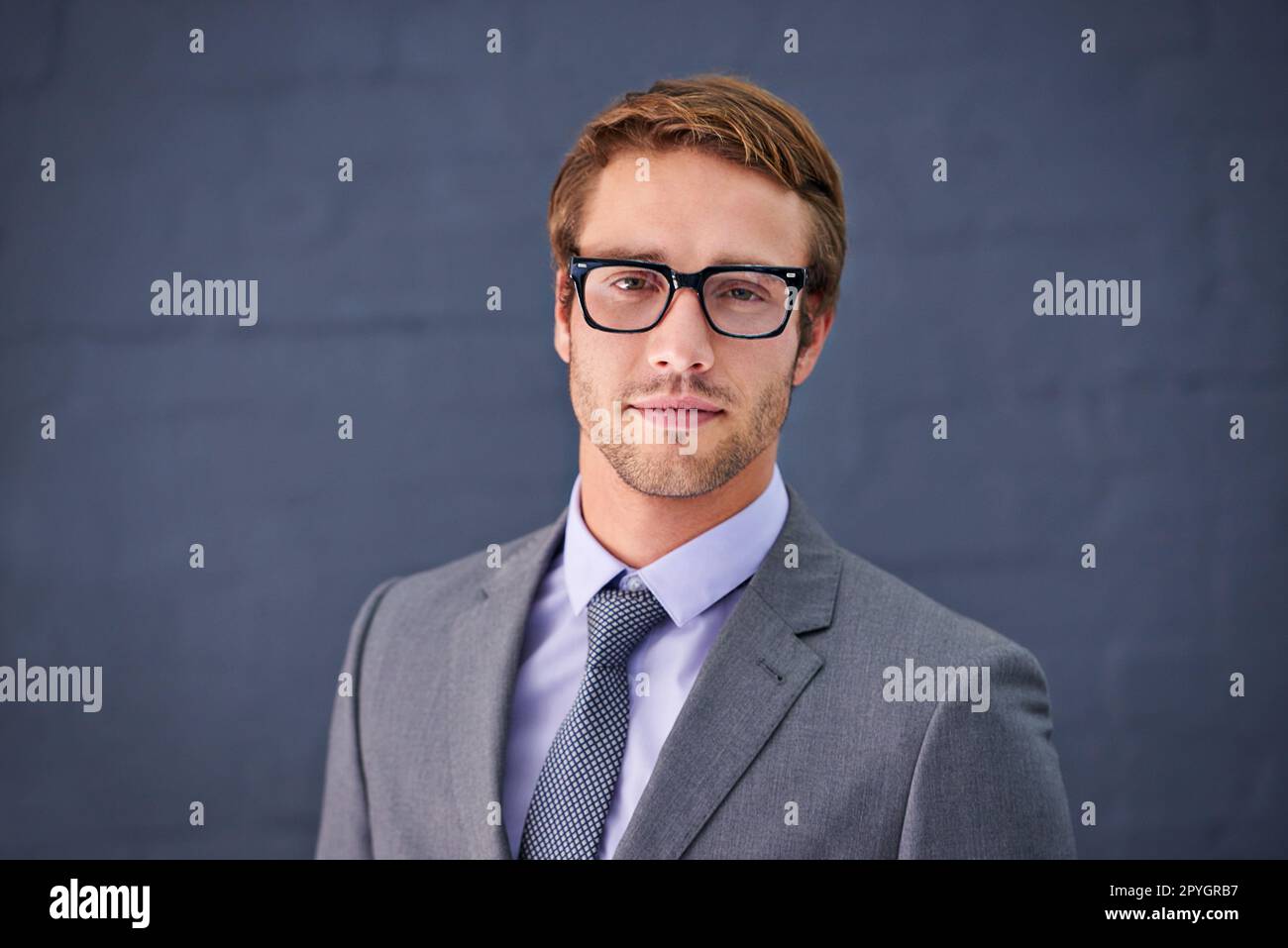 HES élégant et réussi. Portrait d'un beau jeune homme d'affaires debout sur fond gris. Banque D'Images