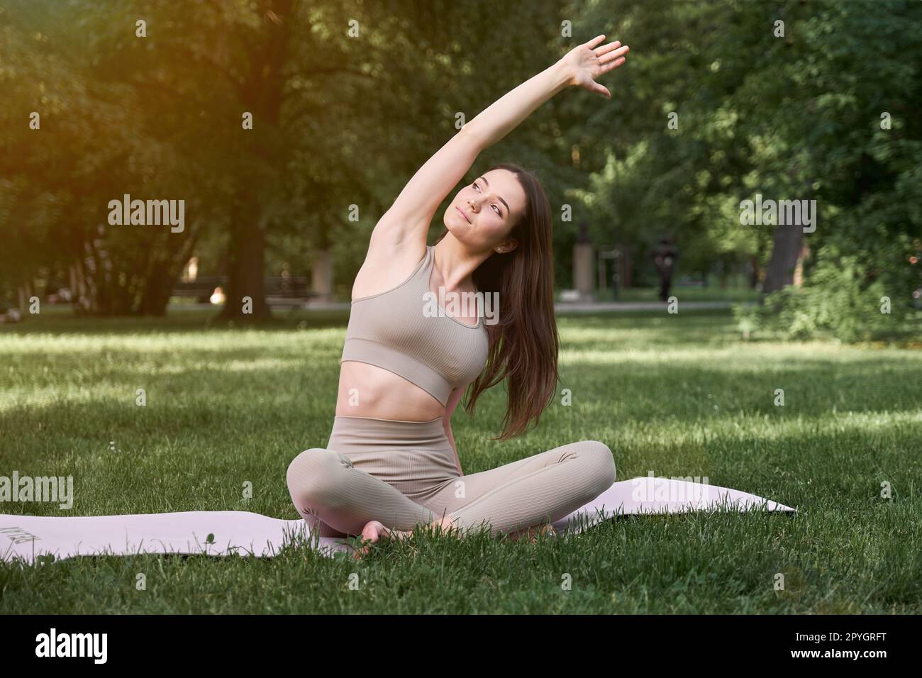Jeune belle femme pratiquant le yoga à l'extérieur dans le parc assis sur un tapis. Banque D'Images