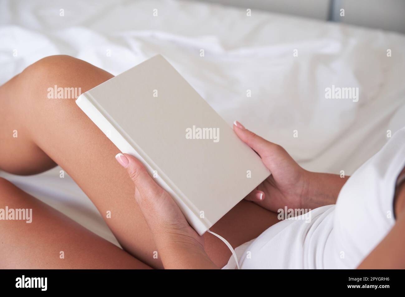 Jeune femme tenant un carnet vierge ou une maquette de livre avec une couverture blanche tout en étant assise sur le lit. Banque D'Images