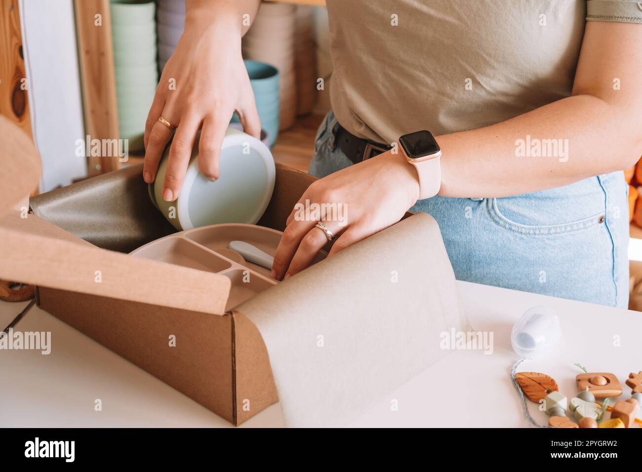 Les mains de femme d'affaires recadrées emballant et emballant l'expédition avec des plats enfants en silicone dans le magasin d'atelier de boîte en carton Banque D'Images