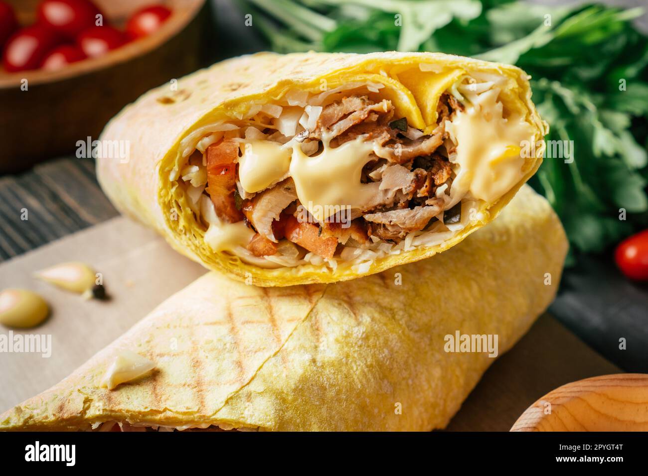Shawarma au fromage avec sauce au fromage, poulet et légumes en pain pita sur surface en bois, tomates cerises et persil Banque D'Images
