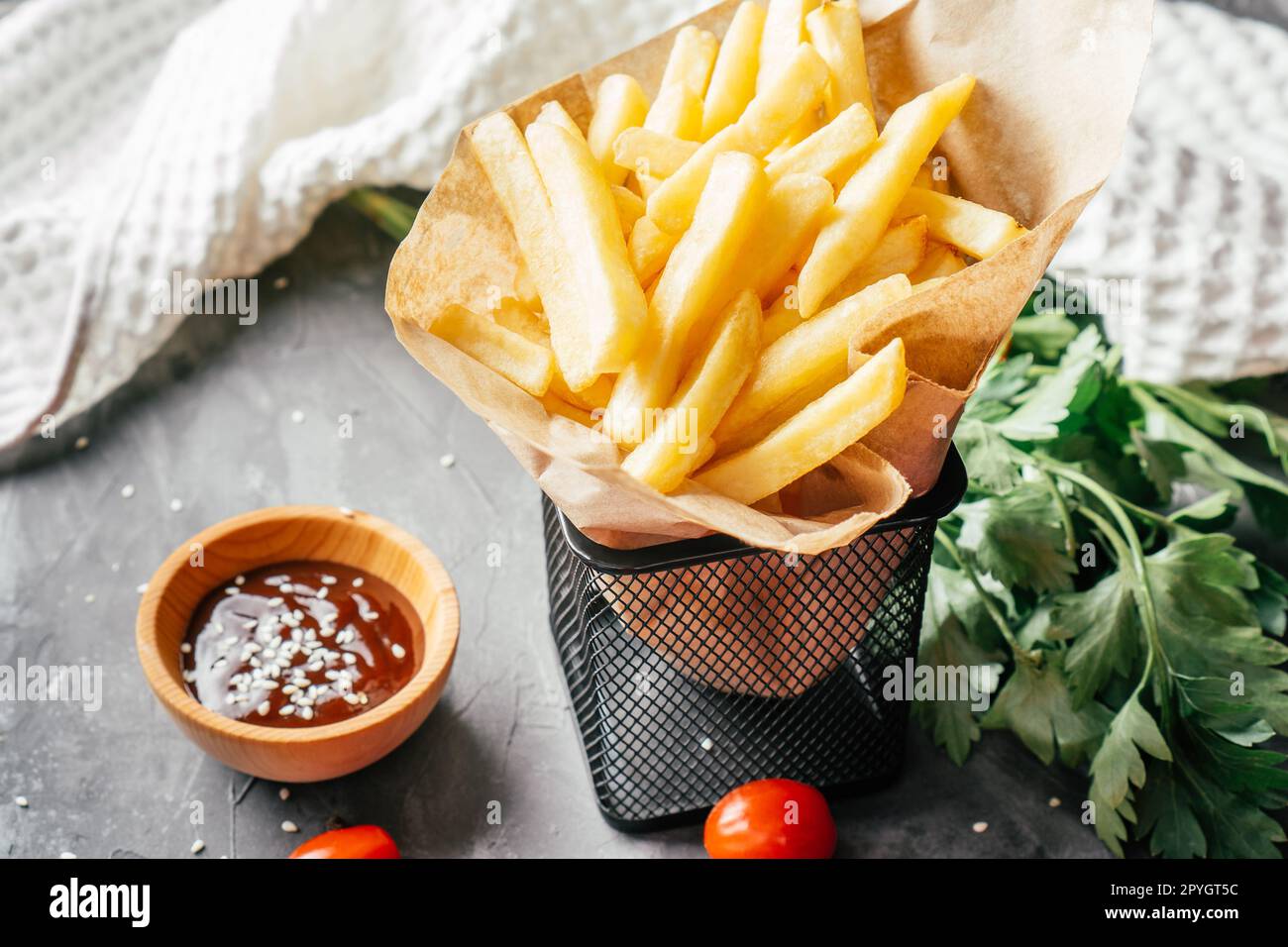 Grande portion de frites en papier artisanal avec sauce barbecue, graines de sésame, tomates cerises et persil vert Banque D'Images