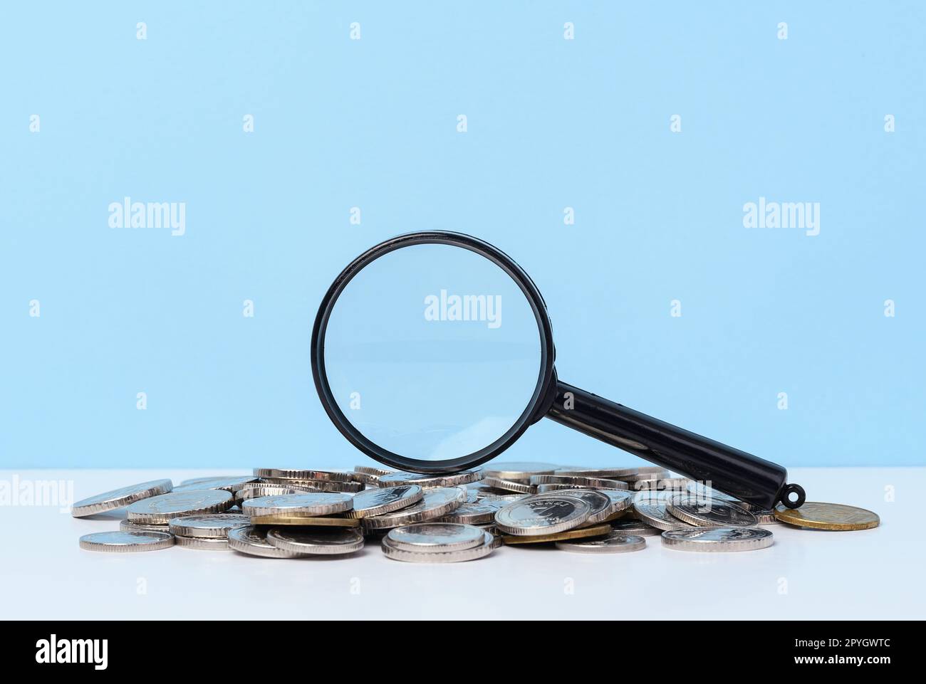 Une pile de pièces de monnaie en métal et une loupe en plastique sur fond bleu. Le concept de l'augmentation des impôts, des subventions Banque D'Images