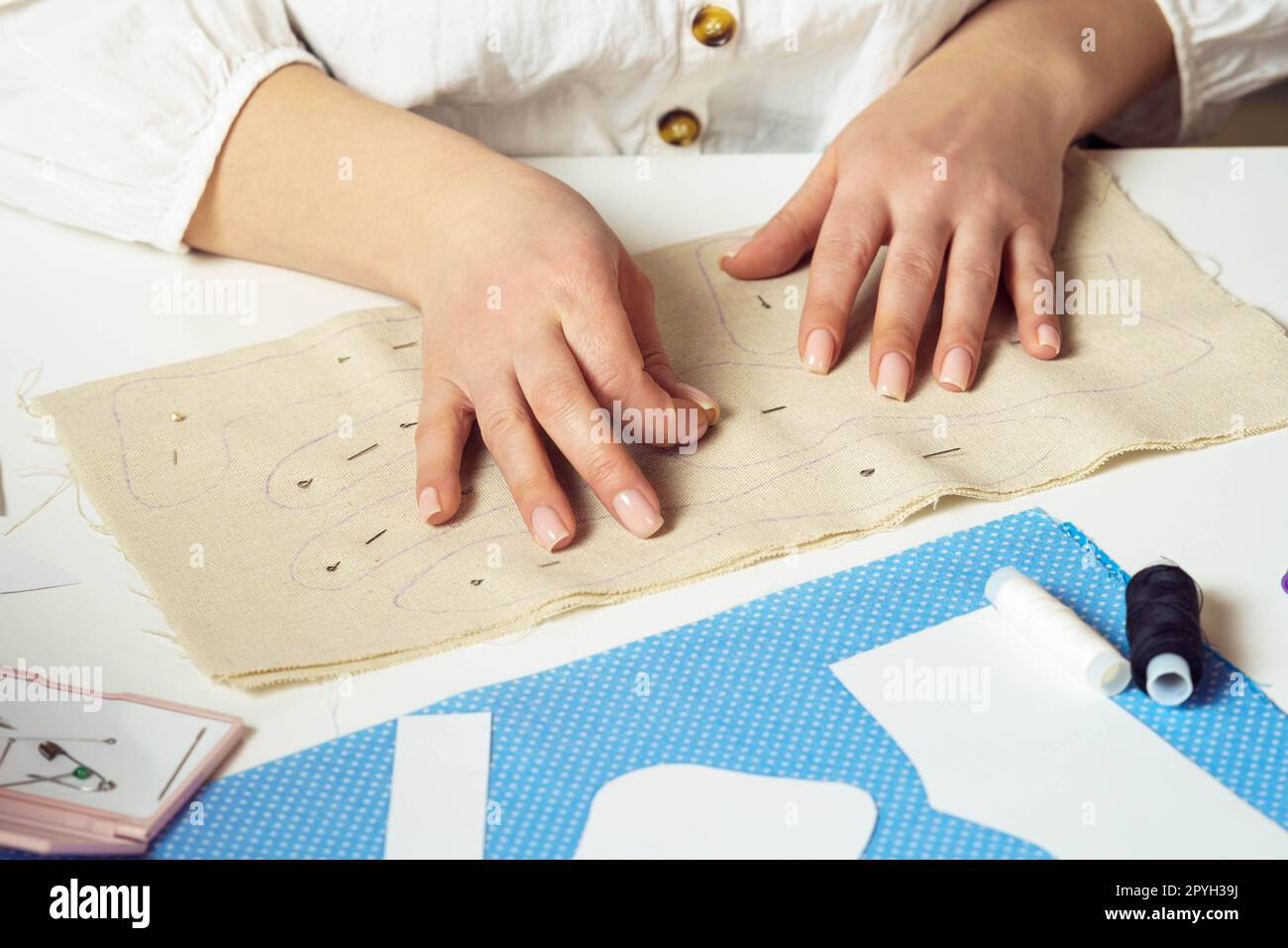 Mains couturières de femme coupée épinglant et faisant des patrons de couture sur la feuille textile sur la table. Travaux d'aiguille, couture de fil Banque D'Images