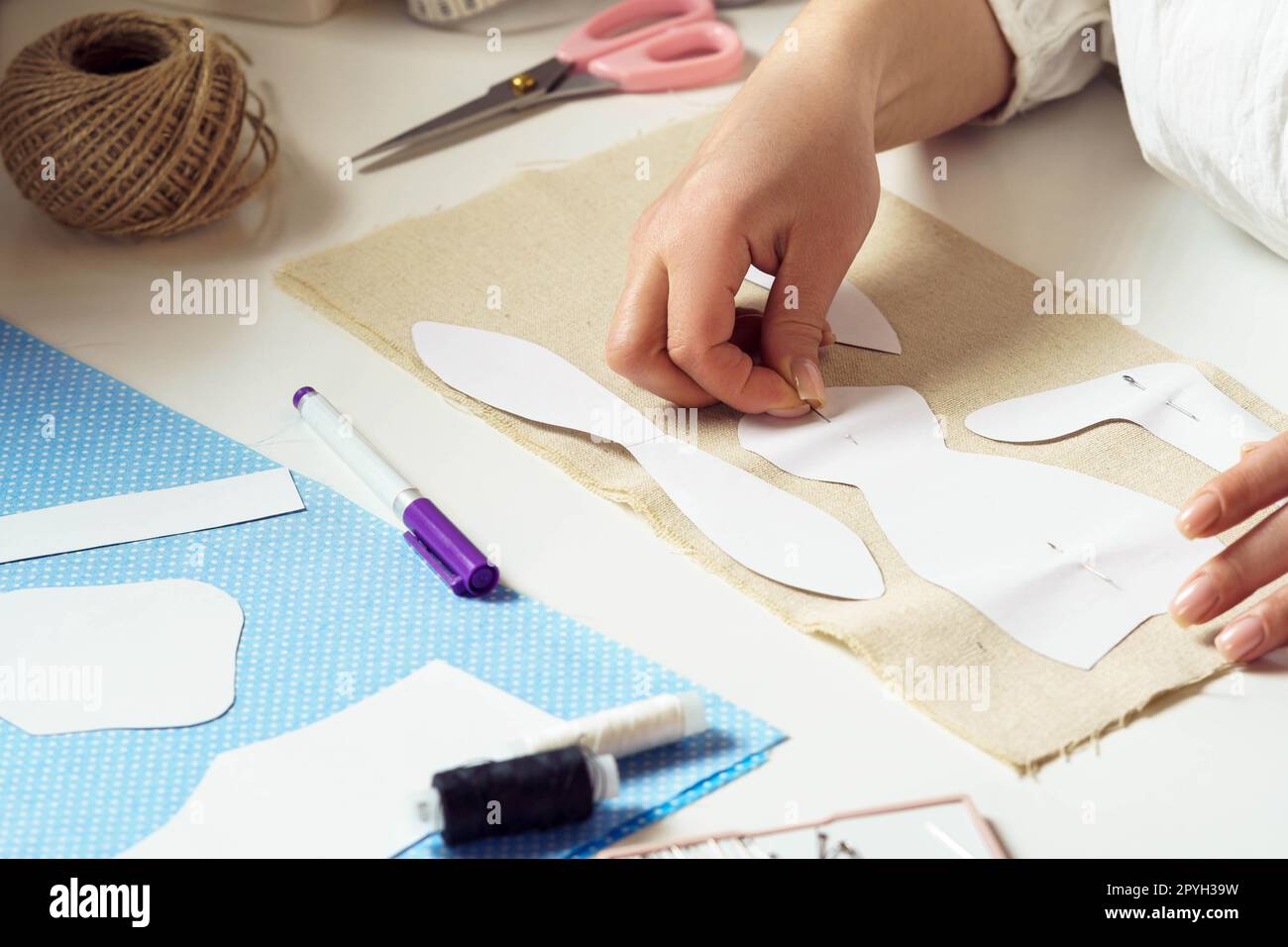 Les mains féminines recadrées prennent des mesures et épinglent des patrons de couture de papier à une feuille textile sur la table. Fil à broder Banque D'Images