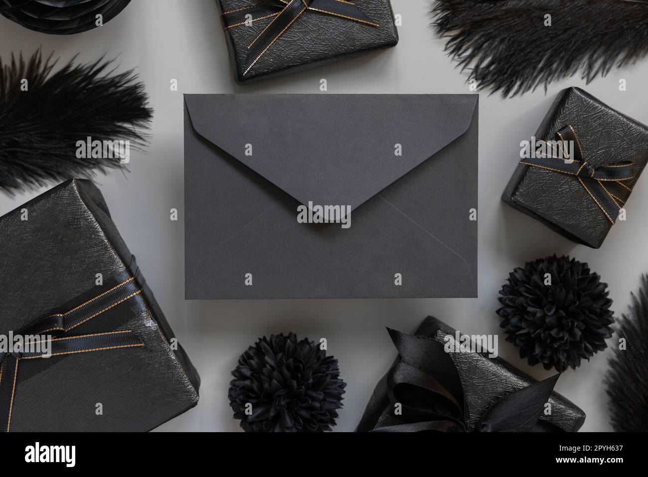 Enveloppe noire entre boîtes cadeaux emballées, fleurs et plumes en papier noir, maquette Banque D'Images