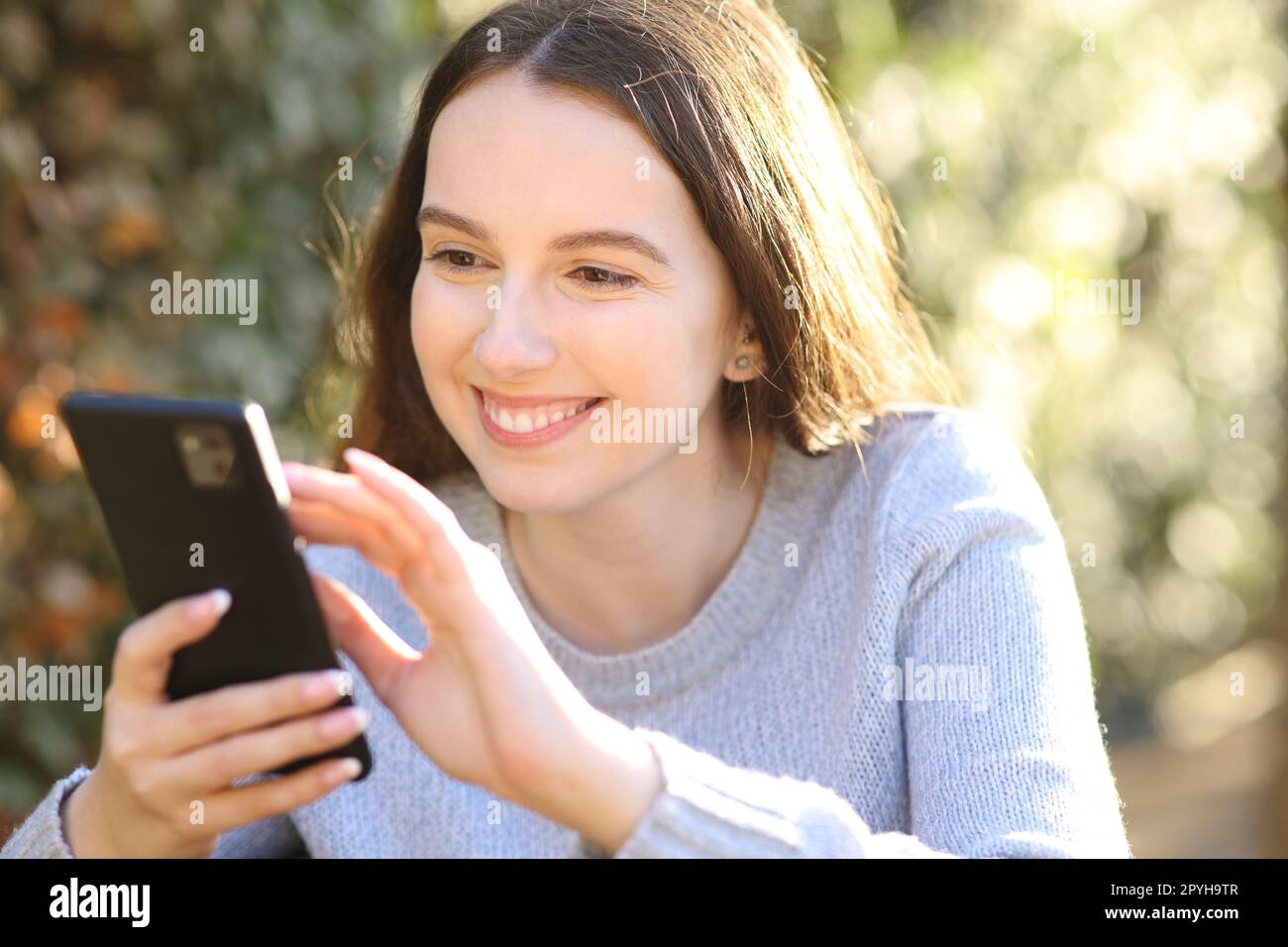 Femme heureuse utilisant un téléphone intelligent dans un parc Banque D'Images