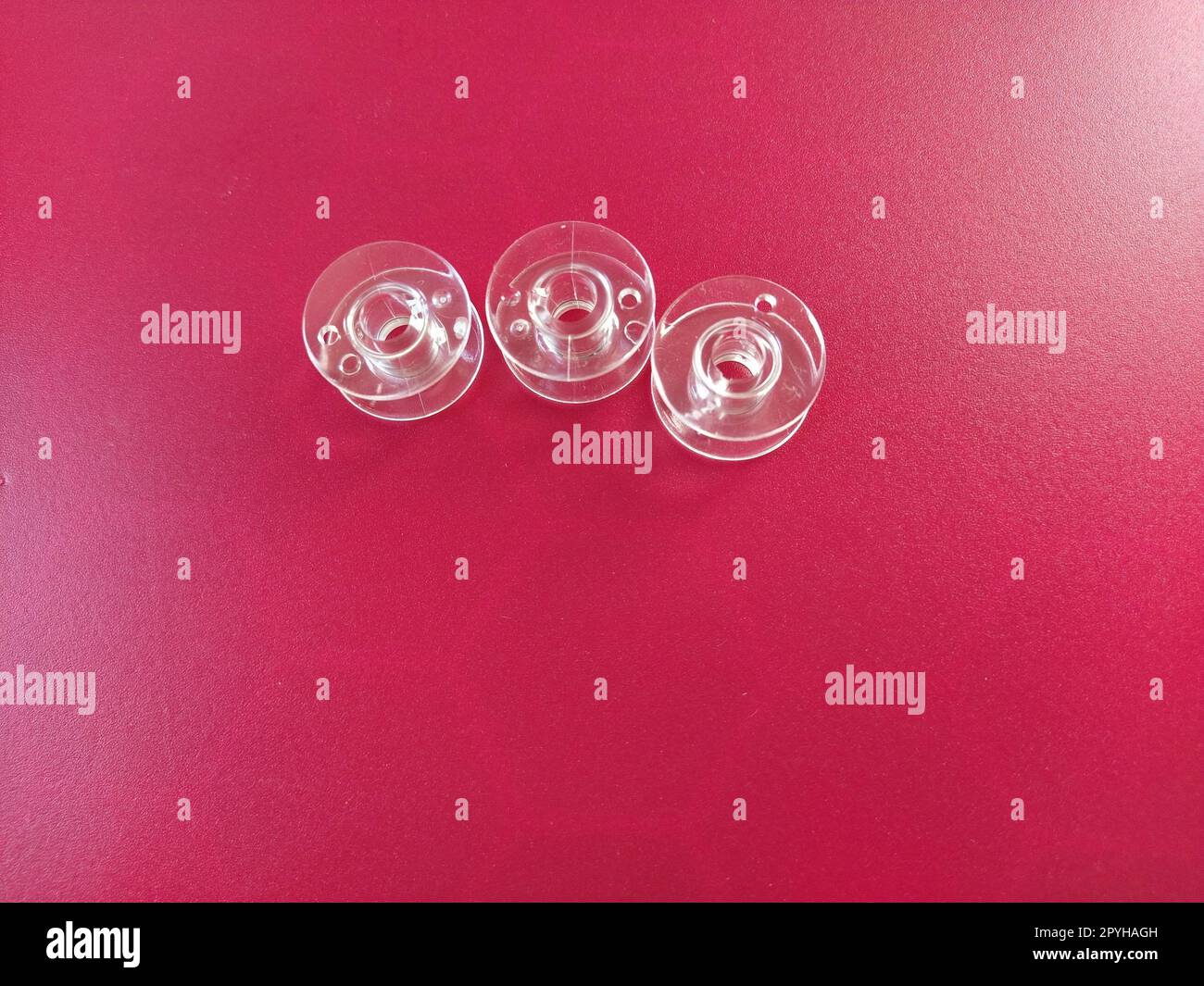 Trois bobines de machine à coudre en plastique transparent. Industrie textile. Détail de l'équipement de couture. Fond rouge Banque D'Images