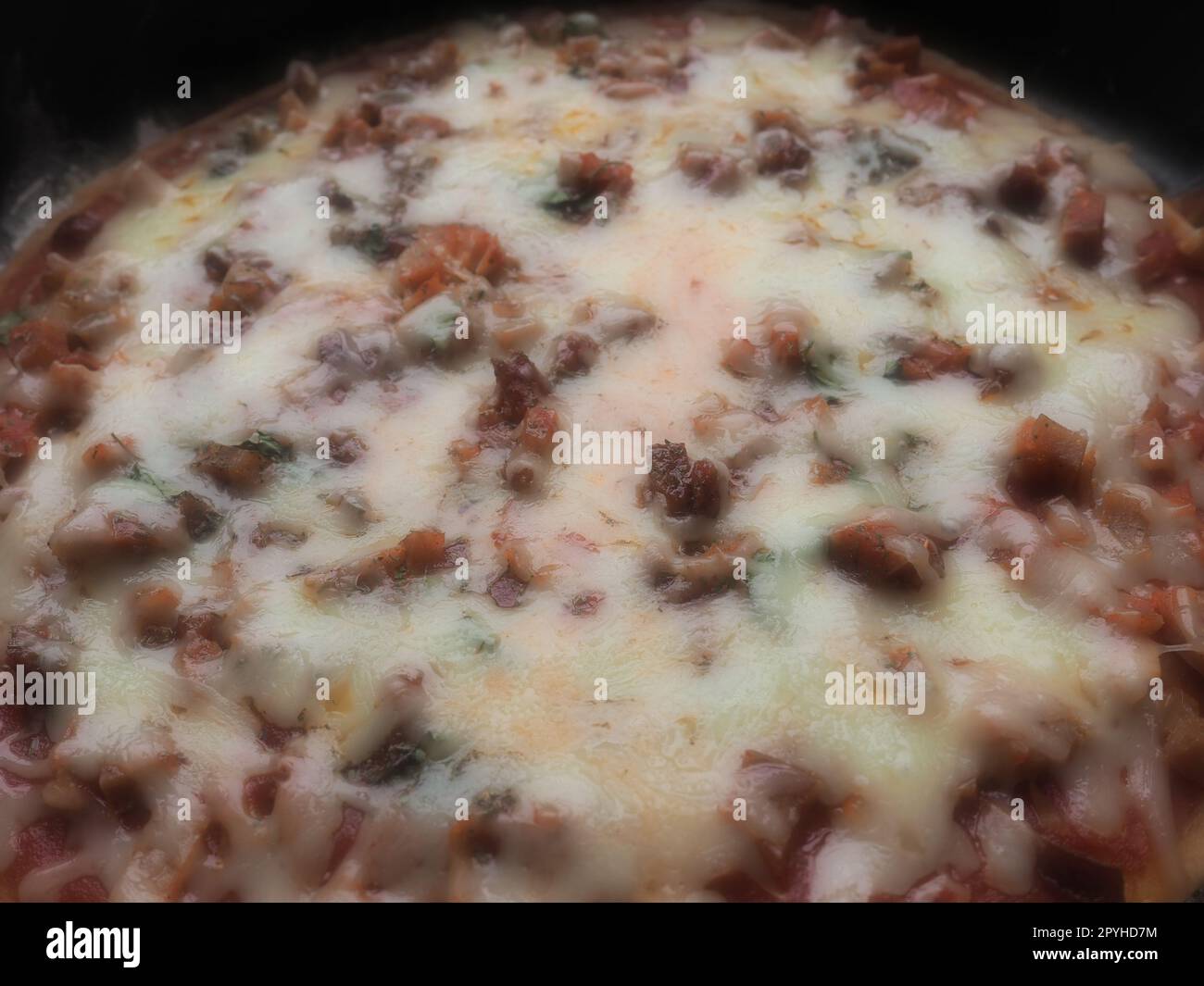 pizza entière en gros plan. Pizza ronde délicieuse et juteuse avec tomates, salami. Le fromage fondu se déverse sur la surface du gâteau cuit au four. Lampe de comptoir. Mise au point floue douce Banque D'Images