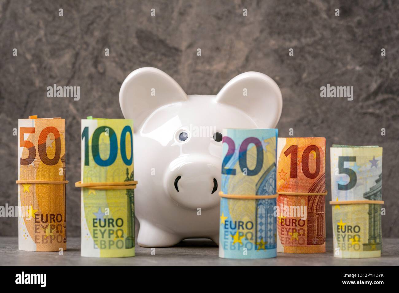 Une tirelire regardant à travers une rangée de billets en euros roulés. Banque D'Images