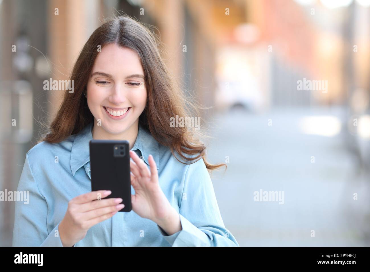 Heureuse femme élégante vérifiant le téléphone intelligent dans la rue Banque D'Images