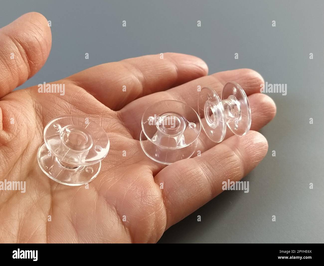 Bobines en plastique transparent d'une machine à coudre moderne dans la paume d'une femme - une couturière. Fond gris. machines à coudre Banque D'Images