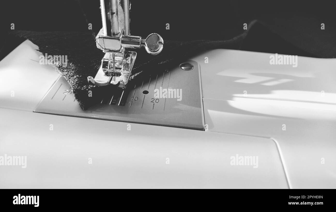 Processus de couture sur une machine à coudre moderne, gros plan. Pied de machine à coudre avec aiguille. Le tissu bleu foncé est garni d'un double emballage du bord du tissu. Lumière naturelle du soleil Banque D'Images