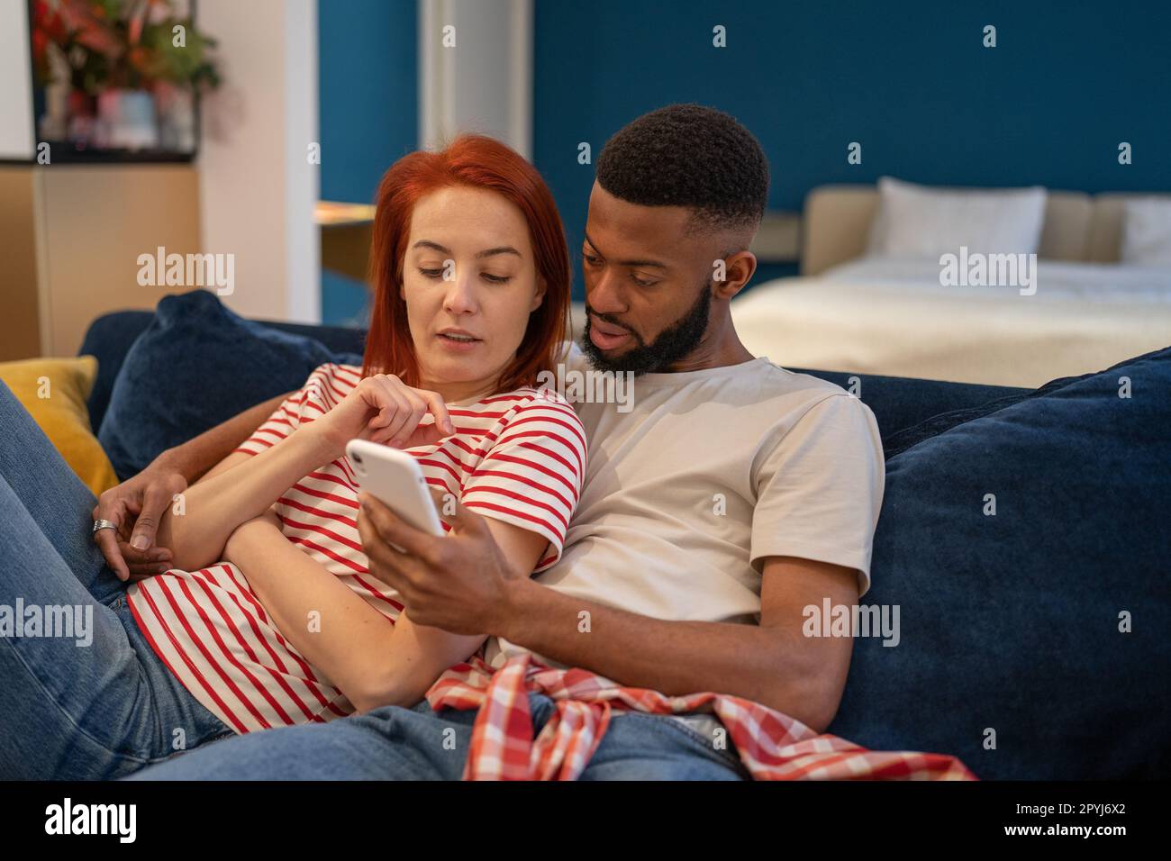 Jeune millénaire couple divers homme et femme se reposant à la maison avec le téléphone mobile Banque D'Images