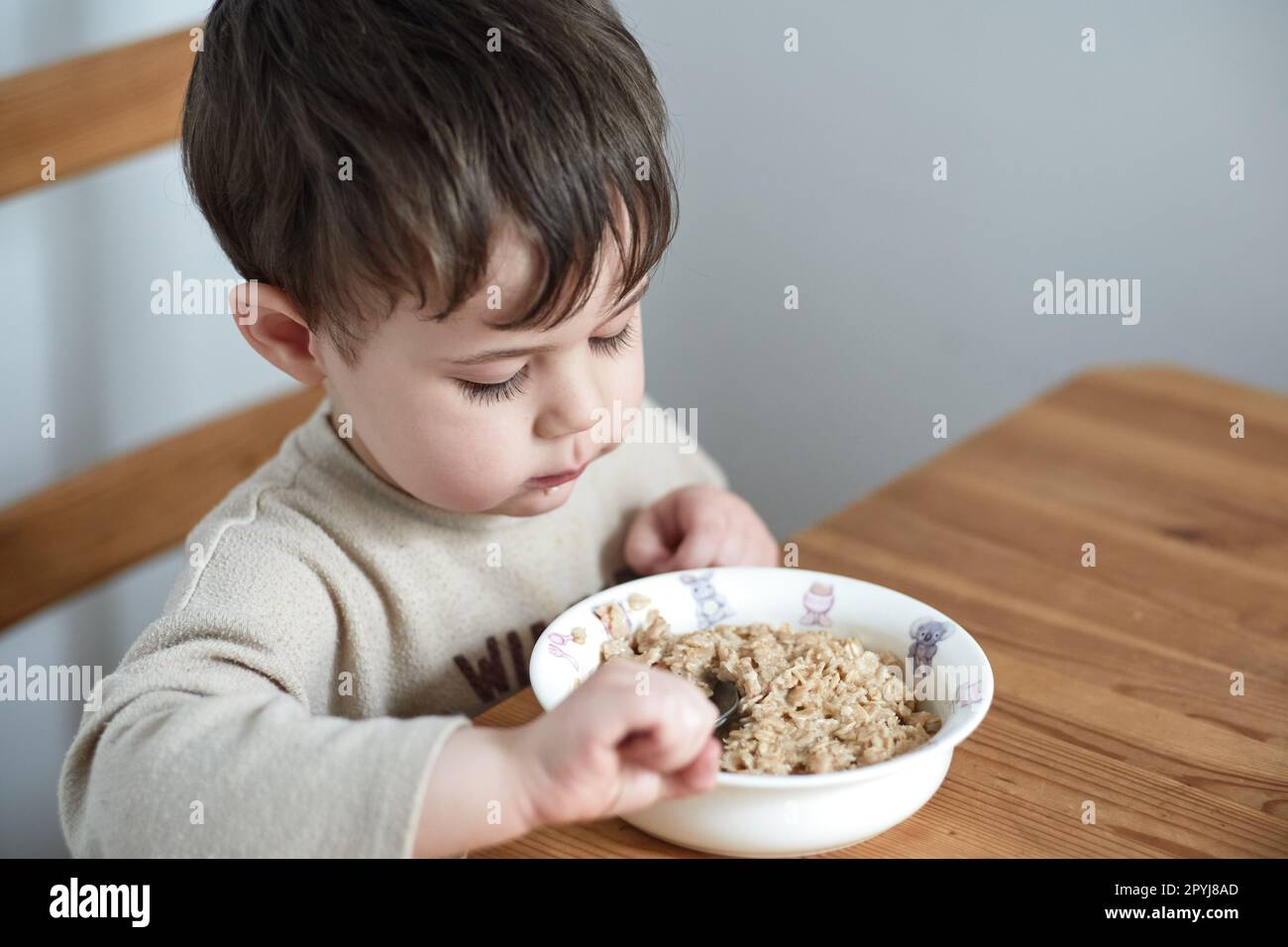 un petit garçon mange des flocons d'avoine pour le petit-déjeuner dans la cuisine Banque D'Images