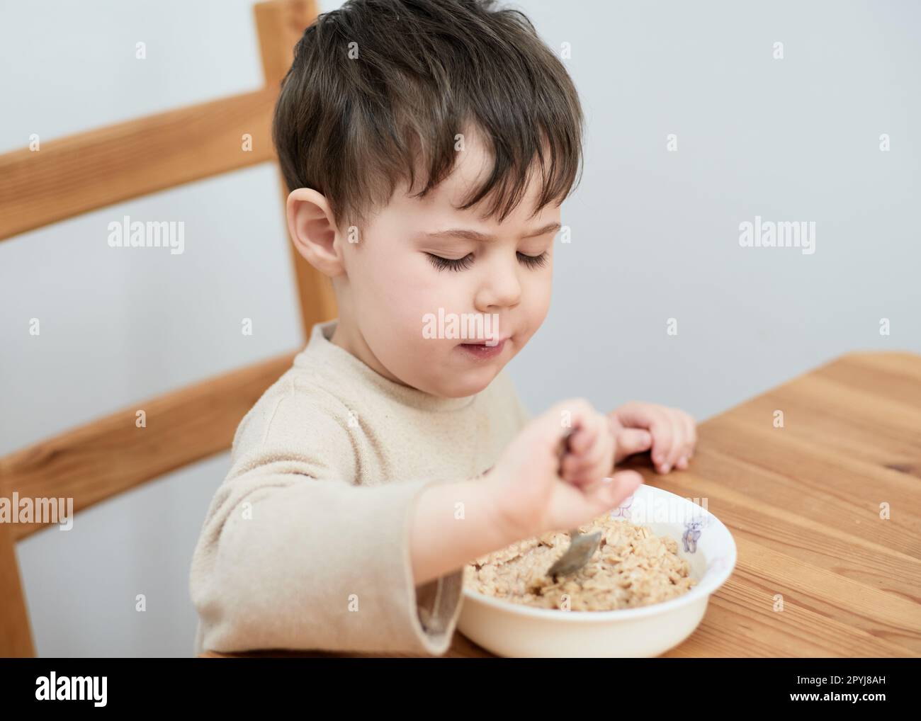 un petit garçon mange des flocons d'avoine pour le petit-déjeuner dans la cuisine Banque D'Images