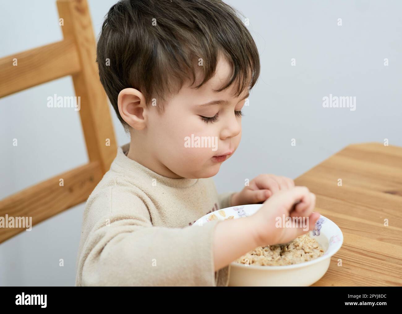 un petit garçon mange des flocons d'avoine pour le petit-déjeuner dans la cuisine Banque D'Images