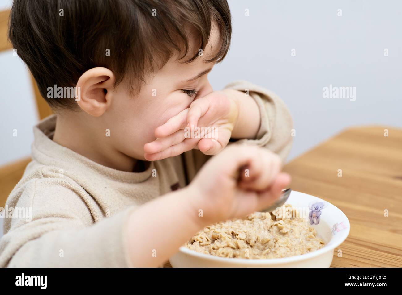 un petit garçon mange des flocons d'avoine pour le petit-déjeuner dans la cuisine Banque D'Images