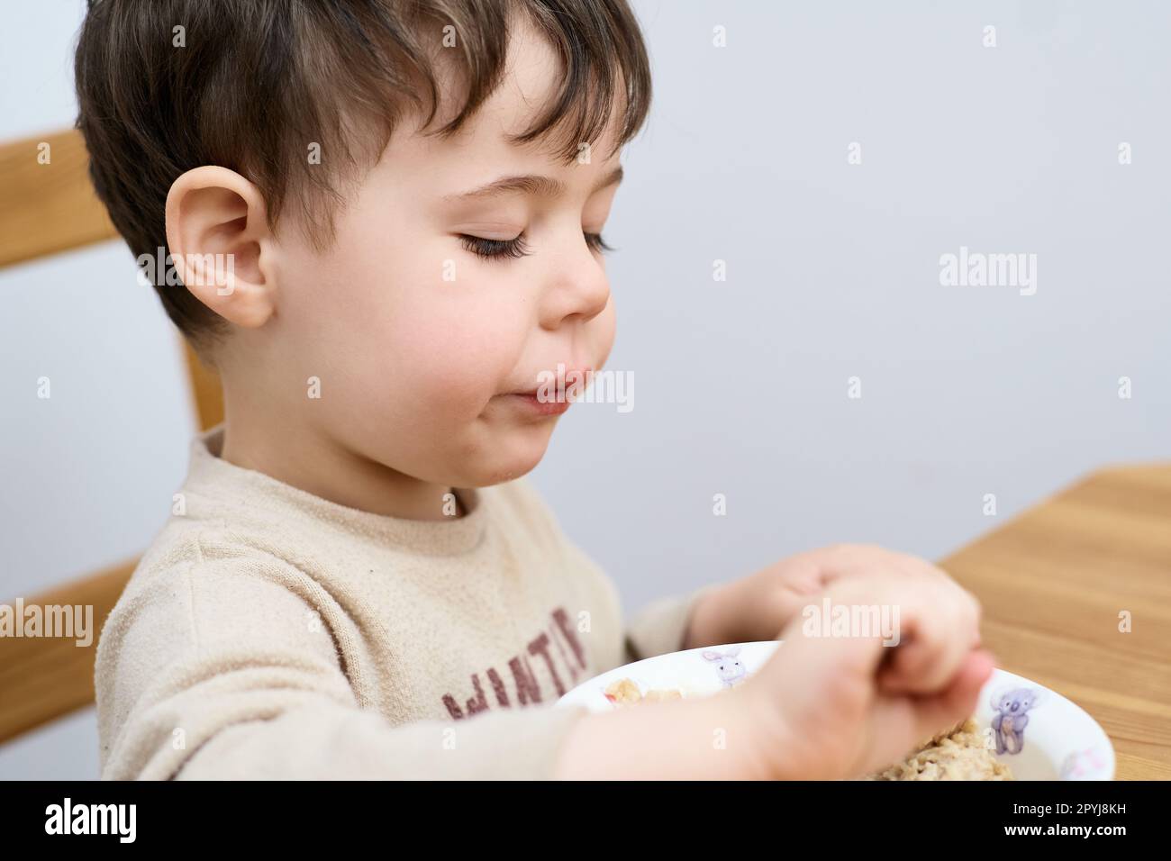 un petit garçon mange des flocons d'avoine pour le petit-déjeuner dans la cuisine Banque D'Images