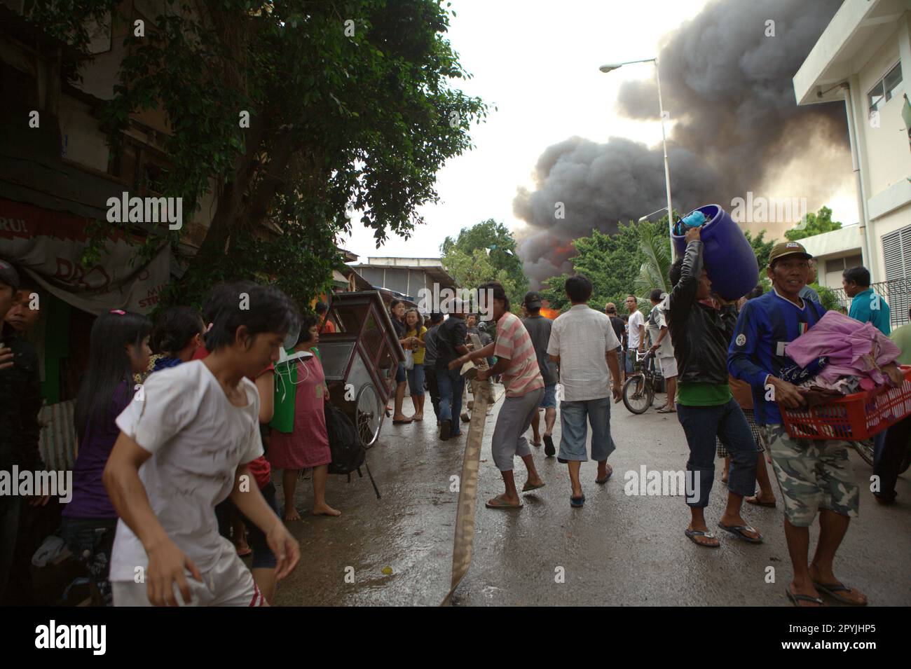 Les gens de la région qui tentent d'aider avec le tuyau d'incendie tandis que d'autres portent leurs effets personnels en raison d'un accident d'incendie brûle un quartier dense à Penjaringan, dans le nord de Jakarta, Jakarta, Indonésie. Banque D'Images