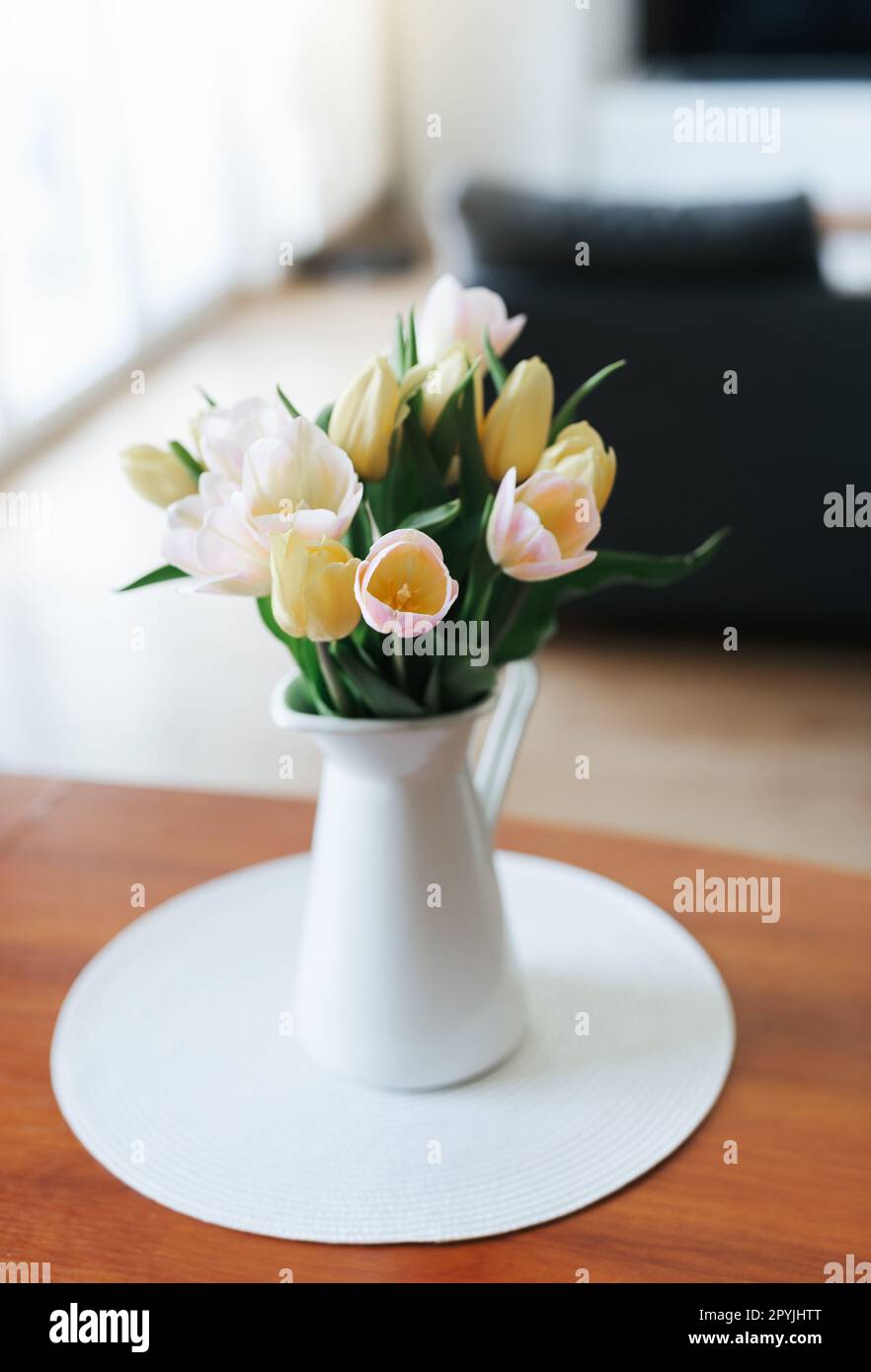 Un bouquet de tulipes dans un vase blanc debout sur la table en bois à l'intérieur. Banque D'Images