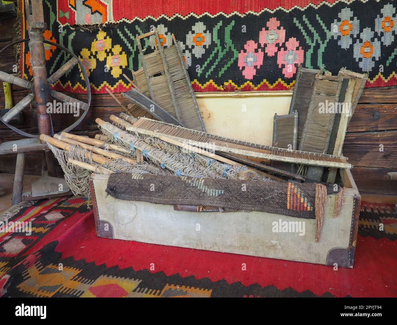 Outils de tissage de tapis anciens. Tissage de tapis en Serbie et en Bosnie. Coffre de bricolage avec cadres en bois, roue de rotation des pieds. Mur de maison en rondins avec des tapis colorés. Travail à thème paysan antique et passe-temps Banque D'Images