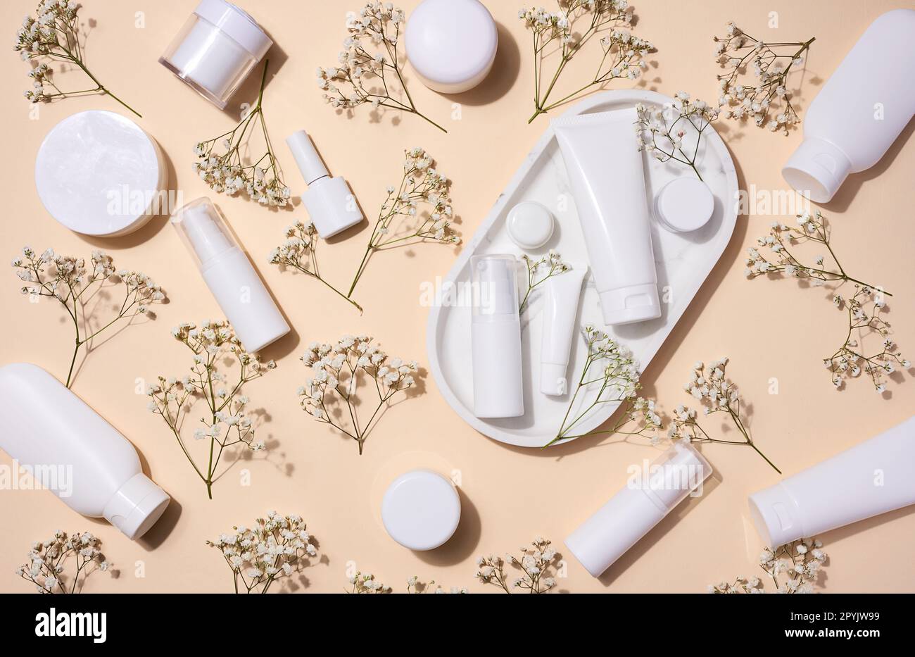 Tubes en plastique blanc, pots et branches de gypsophila sur fond beige, récipients pour crèmes et gels cosmétiques, publicité et promotion de la marque, vue de dessus Banque D'Images