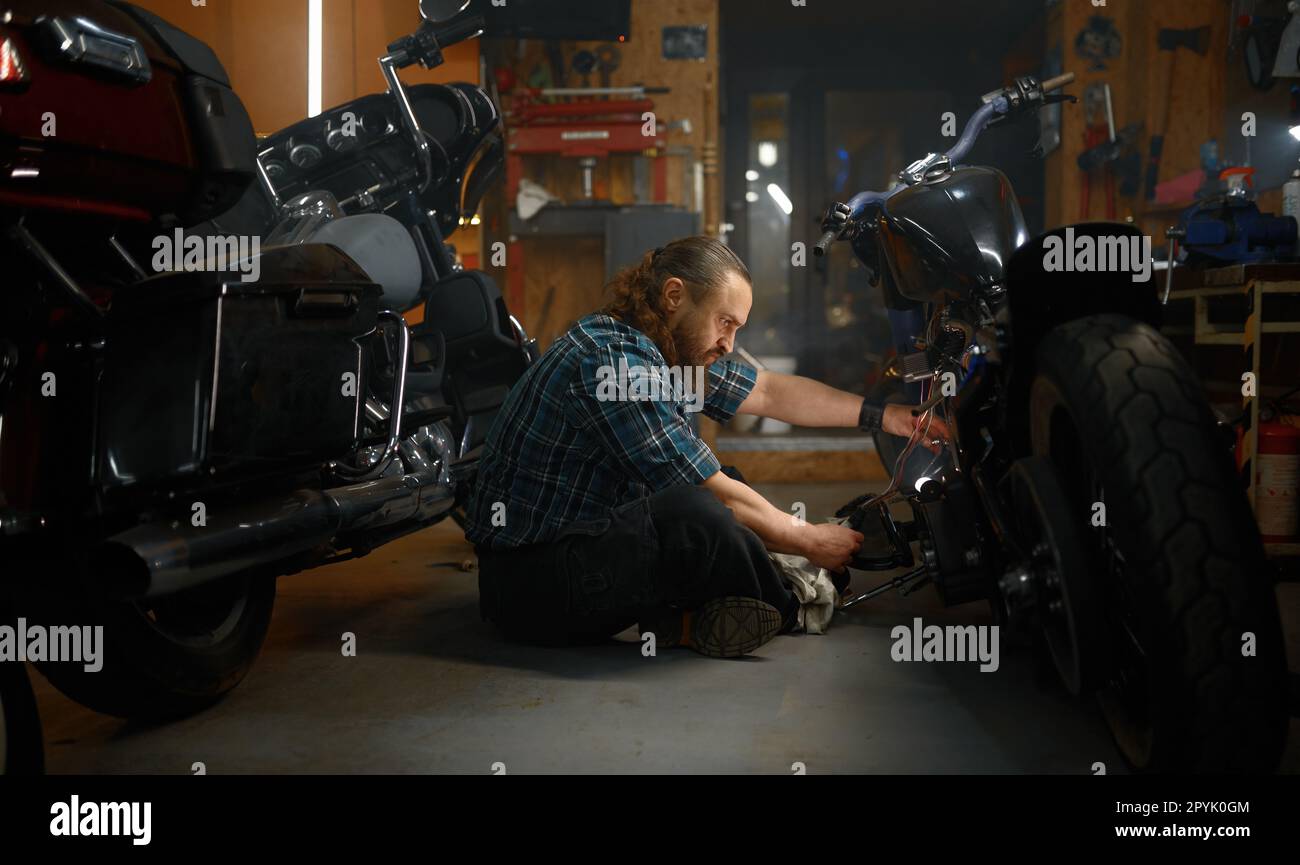 Homme mature cycliste réparant la moto dans le garage le soir Banque D'Images