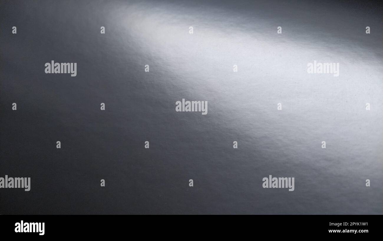 Long éclat de lumière sur papier gris brillant. Point lumineux sur une surface monochrome qui réfléchit la lumière. Fond monochrome abstrait. Bande de haut à gauche à droite en bas Banque D'Images