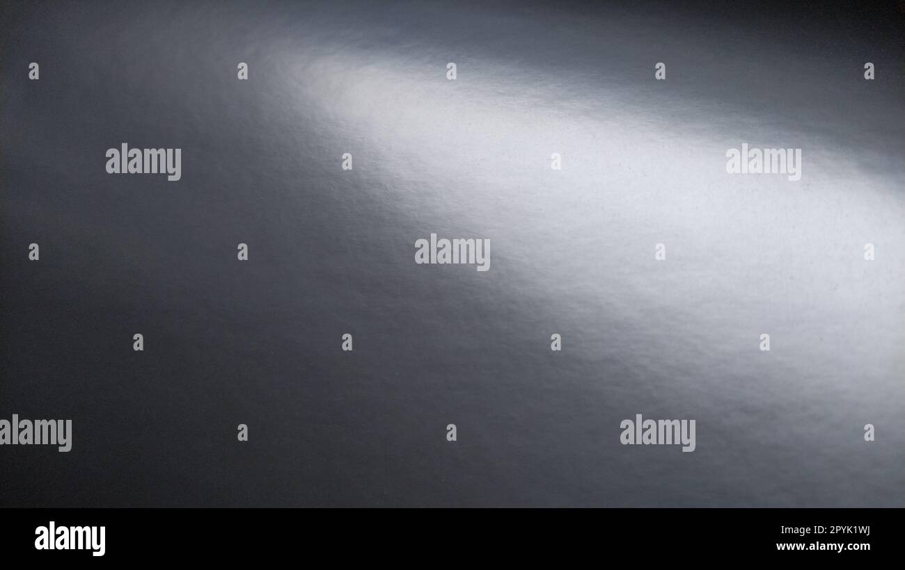 Long éclat de lumière sur papier gris brillant. Point lumineux sur une surface monochrome qui réfléchit la lumière. Fond monochrome abstrait. Bande de haut à gauche à droite en bas Banque D'Images