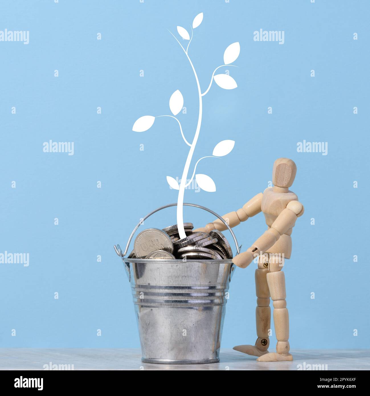 Un mannequin en bois et un seau miniature avec des pièces de monnaie en métal et un arbre peint avec des feuilles sur fond bleu. Concept de croissance des revenus et des bénéfices Banque D'Images