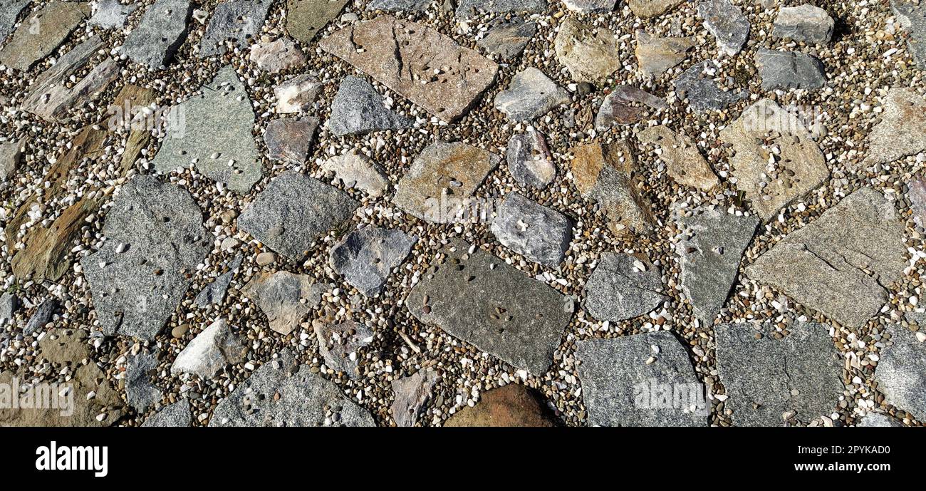 chaussée pavée de pierres grises et brunes naturelles inégales. Entre les pavés broyés, il y a de petits cailloux, de la terre, du sable, de l'herbe. Éclairage solaire. Place dans la vieille ville européenne Banque D'Images